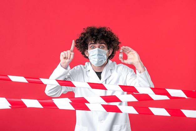 Vooraanzicht mannelijke arts met kolf met medicijnen op rode achtergrond covid-genezen gezondheid gevaar waarschuwing uniforme quarantaine kleuren medisch
