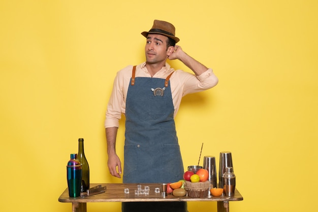 Gratis foto vooraanzicht mannelijke barman die voor het bureau staat met drankjes en fruit poseren op een gele muur drink nachtclub sapbar man