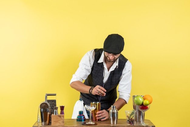 Gratis foto vooraanzicht mannelijke barman voor tafel met shakers die drank bereiden op gele bureaubar alcoholdrank nachtclub jeugd