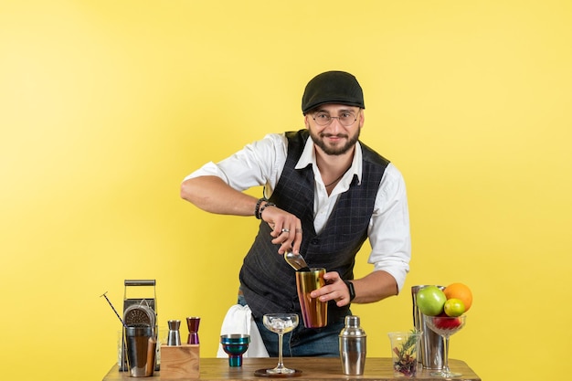 Gratis foto vooraanzicht mannelijke barman voor tafel met shakers die drank bereiden op gele muurbar alcoholdrank nachtclub jeugd