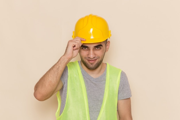 Vooraanzicht mannelijke bouwer in gele helm die eenvoudig op de lichte achtergrond stelt