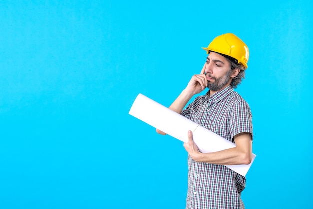 Vooraanzicht mannelijke bouwer in gele helm met plan op een blauwe achtergrond eigendom architectuur aannemer werknemer bouw baan ingenieur