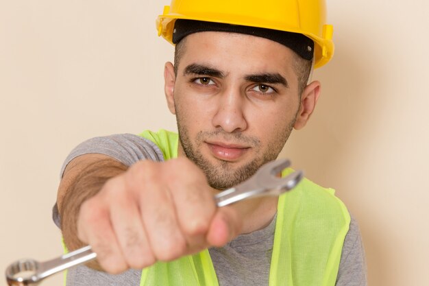 Vooraanzicht mannelijke bouwer in gele helm poseren met zilveren gereedschap op lichte achtergrond