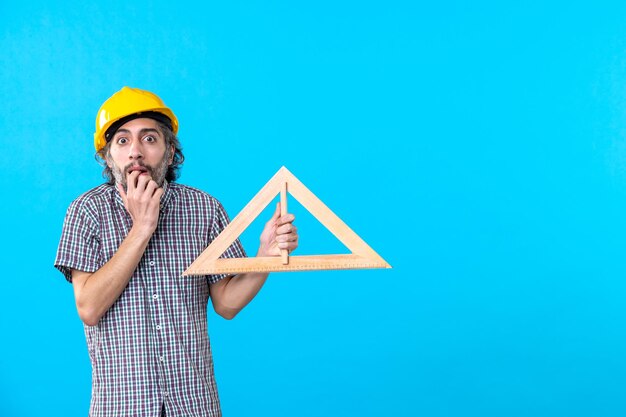 Vooraanzicht mannelijke bouwer in helm met driehoek houten figuur op blauwe achtergrond constructor ontwerp ingenieur architectuur gebouw kleur
