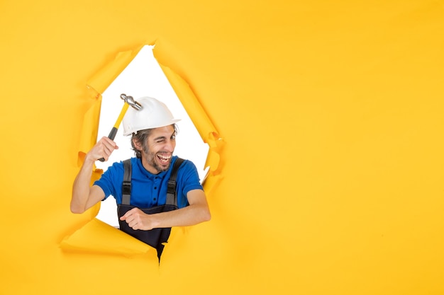 Vooraanzicht mannelijke bouwer in uniform met hamer op gele muur werknemer man bouw baan constructeur architectuur kleur