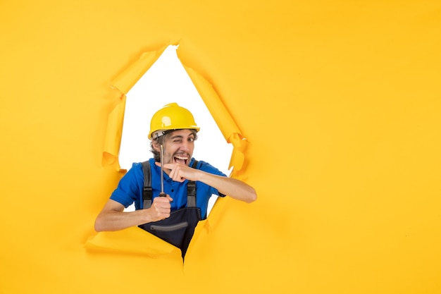 Vooraanzicht mannelijke bouwer in uniform met schroevendraaier op gele muur werk constructeur gebouw kleur baan werknemer architectuur