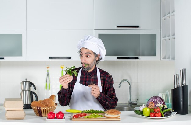 Vooraanzicht mannelijke chef-kok met greens in de keuken