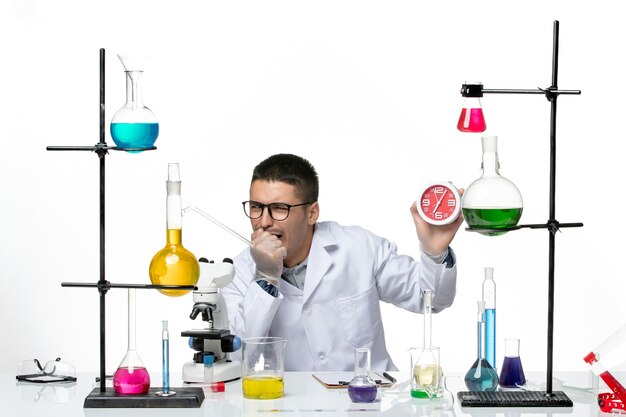 Vooraanzicht mannelijke chemicus in wit medisch pak met klokken op witte achtergrond covid virus ziekte wetenschappelijk laboratorium