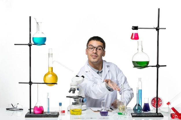 Vooraanzicht mannelijke chemicus in witte medische pak zittend met oplossingen op witte achtergrond virus lab covid ziekte wetenschap