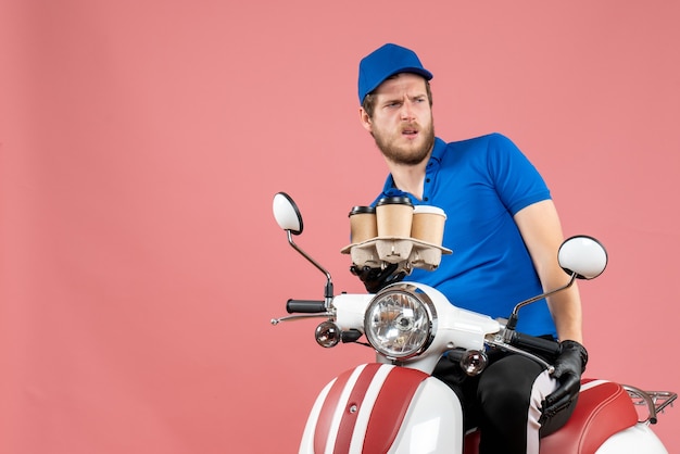 Vooraanzicht mannelijke koerier die op de fiets zit en koffiekopjes op de roze houdt