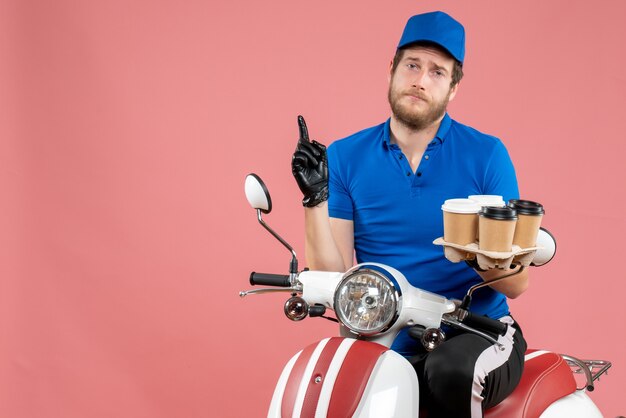 Vooraanzicht mannelijke koerier die op de fiets zit en koffiekopjes op de roze houdt