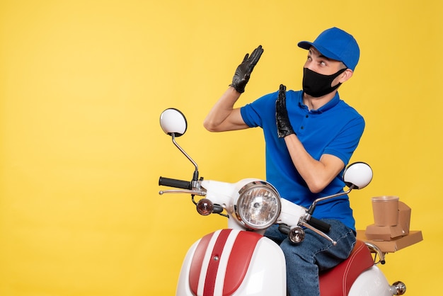 Vooraanzicht mannelijke koerier in blauw uniform en masker op een gele werkvirus covid levering pandemie fietsservicebaan