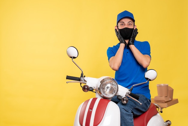 Vooraanzicht mannelijke koerier in blauw uniform en masker op geel virus baan fiets covid-bezorgdienst werk