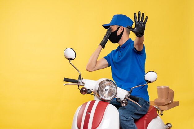 Vooraanzicht mannelijke koerier in blauw uniform en masker op gele pandemie werk covid-service job virus fiets levering