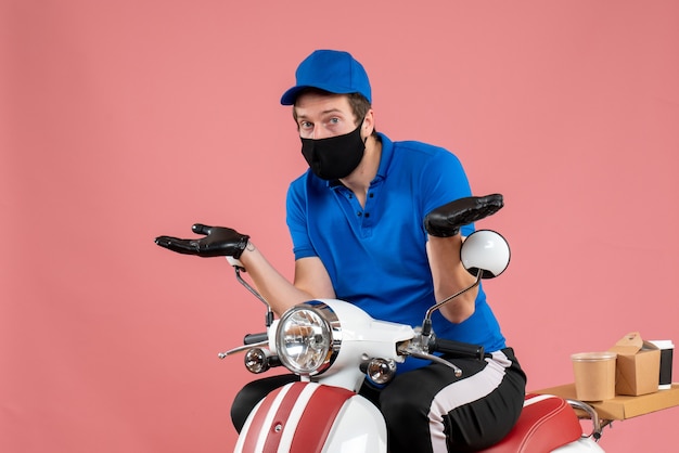 Vooraanzicht mannelijke koerier in blauw uniform en masker op roze baanbezorging fastfood fietswerk covid voedselvirusservice