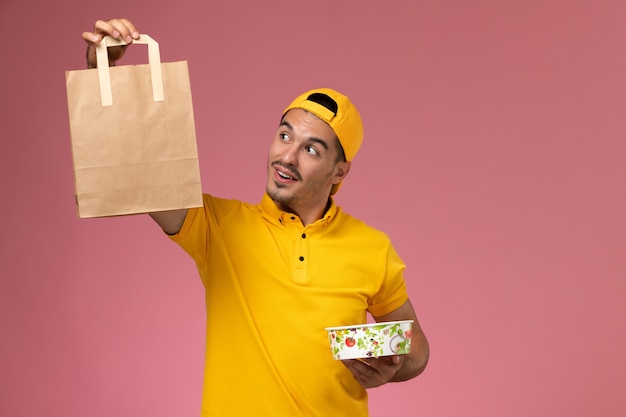 Vooraanzicht mannelijke koerier in de gele uniforme kom van het het voedselpakket van de holdingslevering op roze achtergrond.