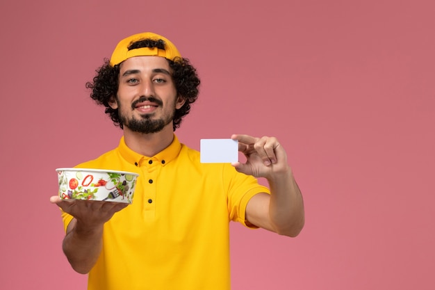 Vooraanzicht mannelijke koerier in geel uniform en cape met ronde leveringskom kaart op zijn handen op de roze achtergrond.