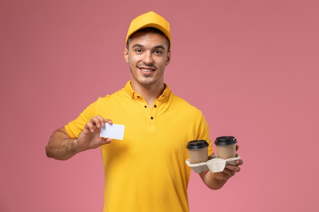 Vooraanzicht mannelijke koerier in geel uniform met grijze kaart en levering koffiekopjes op roze achtergrond