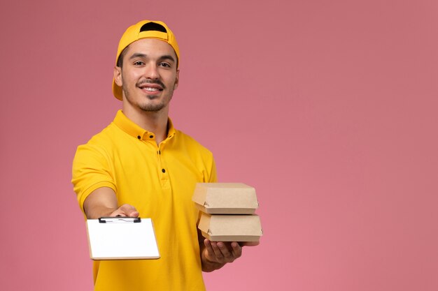 Vooraanzicht mannelijke koerier in geel uniform met kleine voedselpakketten op roze achtergrond.