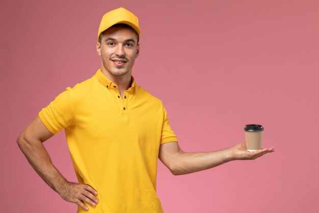 Vooraanzicht mannelijke koerier in gele uniforme koffieleveringskop op het roze bureau te houden