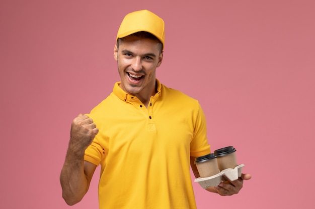 Vooraanzicht mannelijke koerier in gele uniforme levering koffiekopjes houden en vreugde op roze achtergrond