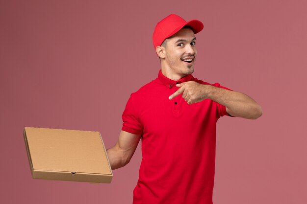 Vooraanzicht mannelijke koerier in rood uniform en cape met voedselleveringsdoos op de roze muurarbeiderbaan