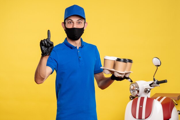 Vooraanzicht mannelijke koerier in zwart masker koffie op gele baan covid-pandemie levering uniforme dienst te houden