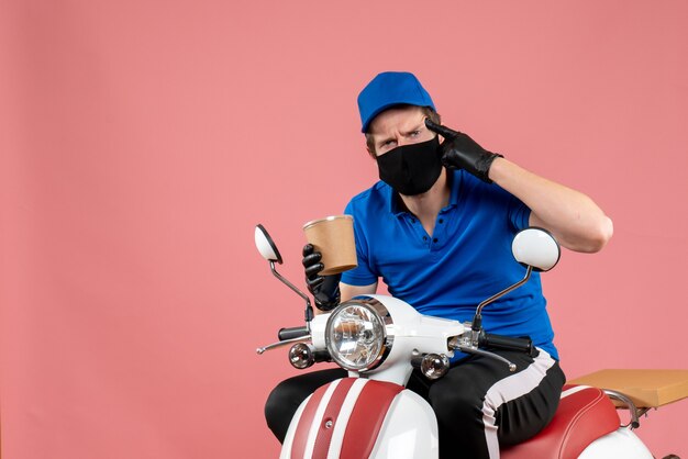 Vooraanzicht mannelijke koerier zittend op de fiets en met een grote koffiekop op de roze