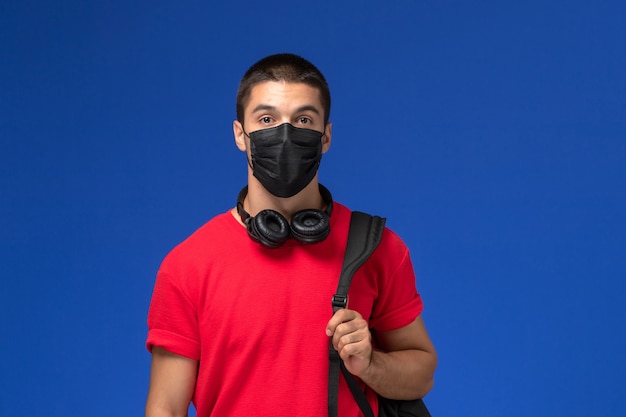 Vooraanzicht mannelijke student in rood t-shirt masker met rugzak dragen op de blauwe achtergrond.