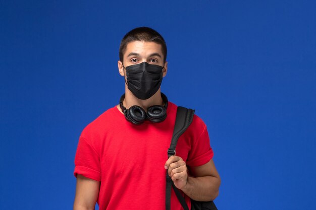 Vooraanzicht mannelijke student in rood t-shirt masker met rugzak dragen op de blauwe achtergrond.