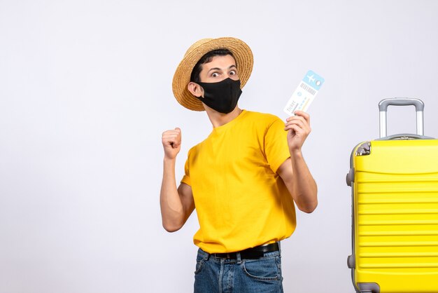 Vooraanzicht mannelijke toerist in gele t-shirt die zich dichtbij gele koffer bevindt die reiskaartje steunt