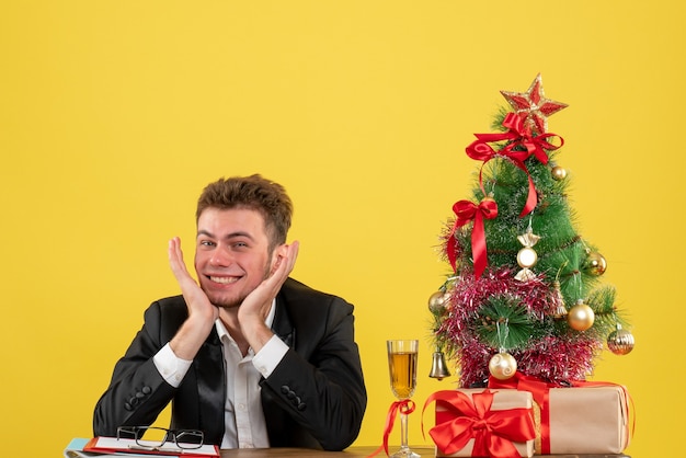 Vooraanzicht mannelijke werknemer achter zijn werkplek met cadeautjes op geel