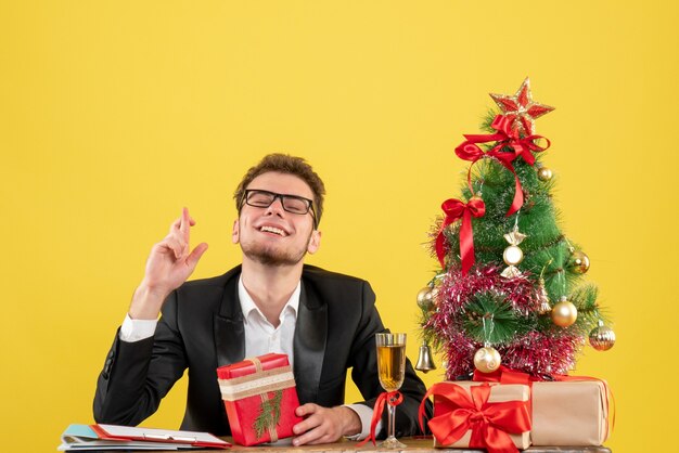 Vooraanzicht mannelijke werknemer achter zijn werkplek met cadeautjes op geel