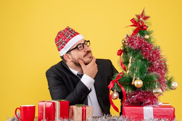 Vooraanzicht mannelijke werknemer achter zijn werkplek met cadeautjes op geel