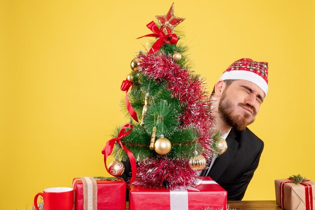 Vooraanzicht mannelijke werknemer achter zijn werkplek met cadeautjes op geel