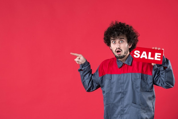 Vooraanzicht mannelijke werknemer met rode verkoop naambord op rode achtergrond monteur foto huis werknemer uniform instrument kleuren winkelen baan