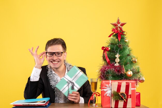 Vooraanzicht mannelijke werknemer zitten met kerstcadeautjes en boom