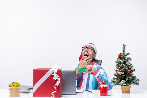 Vooraanzicht mannelijke werknemer zittend op zijn werkplek met groene bankkaart baan emoties kerst kantoor geld