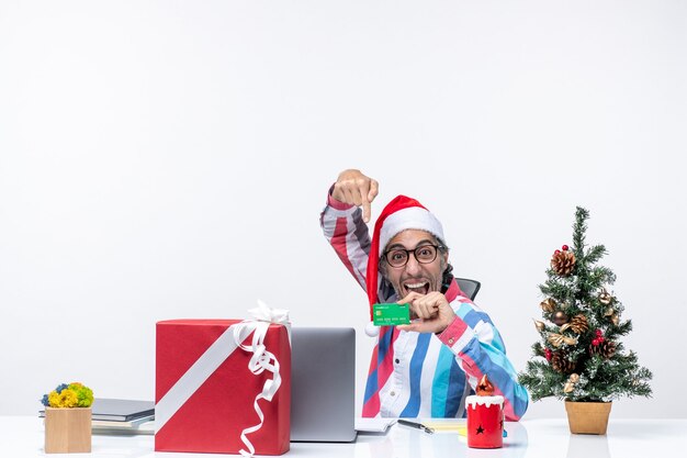 Vooraanzicht mannelijke werknemer zittend op zijn werkplek met groene bankkaart baan foto emotie kerst kantoor geld