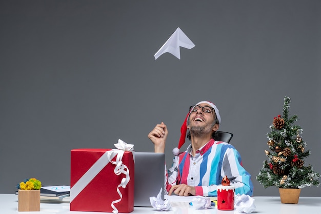 Vooraanzicht mannelijke werknemer zittend op zijn werkplek spelen met papieren vliegtuigje