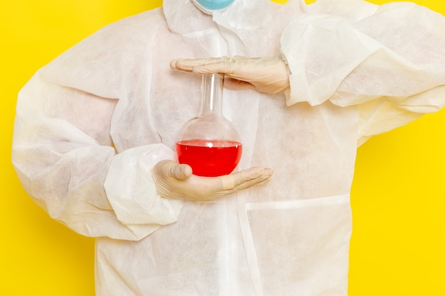Gratis foto vooraanzicht mannelijke wetenschappelijke werker in speciaal beschermend pak bedrijf kolf met rode oplossing op geel oppervlak