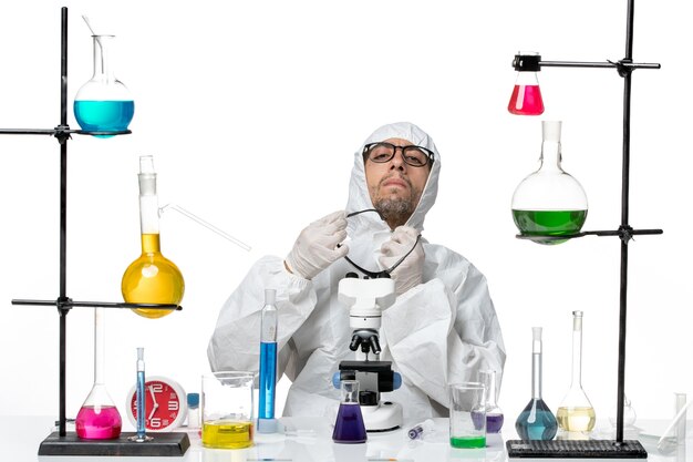 Vooraanzicht mannelijke wetenschapper in speciaal beschermend pak aan tafel zitten met oplossingen