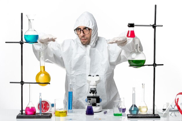 Vooraanzicht mannelijke wetenschapper in speciaal beschermend pak rond tafel met oplossingen