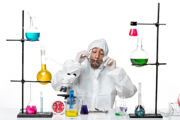 Vooraanzicht mannelijke wetenschapper in speciaal beschermend pak zittend rond een bureau met oplossingen