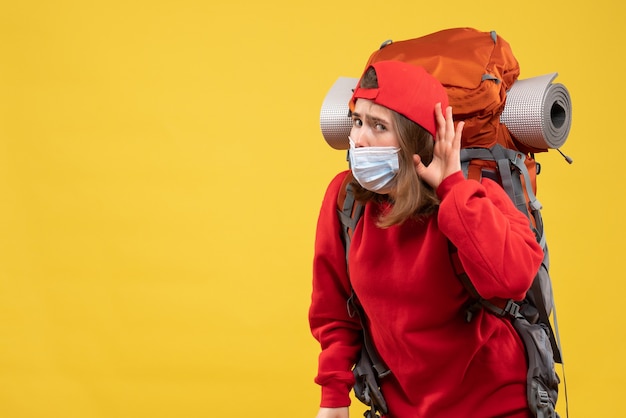 Vooraanzicht nieuwsgierig jong meisje met toeristenrugzak en masker dat naar iets luistert