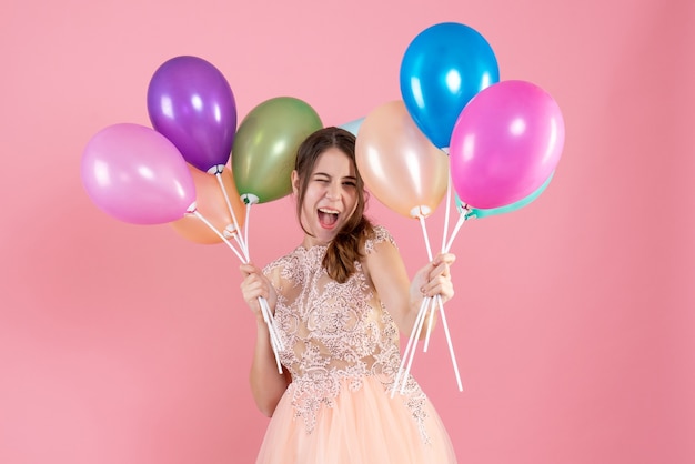 Vooraanzicht opgewonden feestmeisje met feestmuts met ballonnen in de buurt van haar gezicht