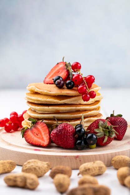 Vooraanzicht pannenkoeken met aardbeien zwarte en rode aalbessen op een dienblad met pinda's