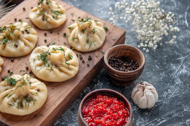 Vooraanzicht rauwe kleine dumplings met tomatensaus en kruiden op de grijze tafel vlees deeg maaltijd cake koken schotel keuken diner