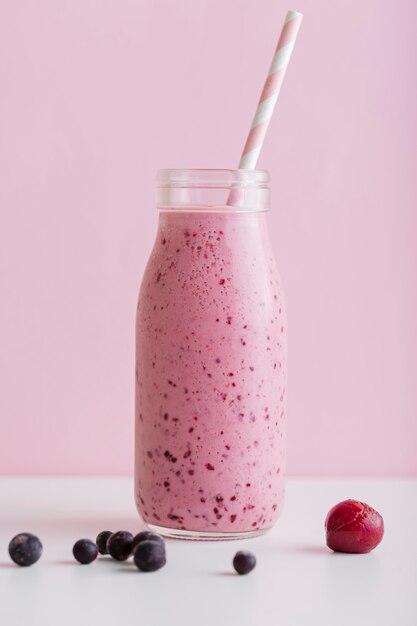 Vooraanzicht roze smoothiefles met stro en bessen