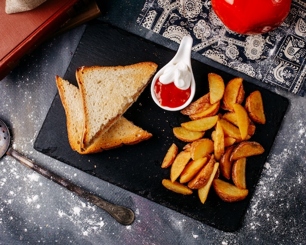 Vooraanzicht sandwiches samen met gebakken aardappelen in zwarte plaat op de grijze vloer